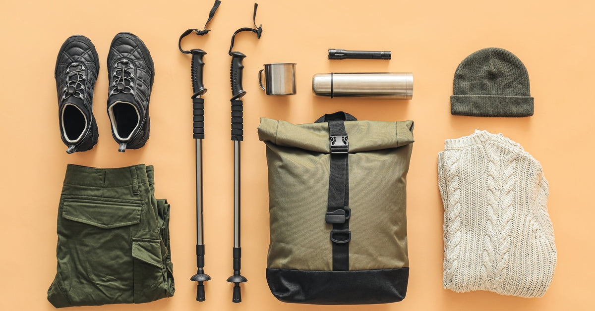 Hiking gear--including a backpack, shoes, trekking poles, a water bottle, a flashlight, and clothing--set on an orange surface.